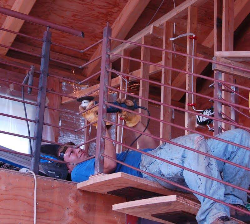 Jesse, the welder, laying on his back grinding on a railing of a staircase