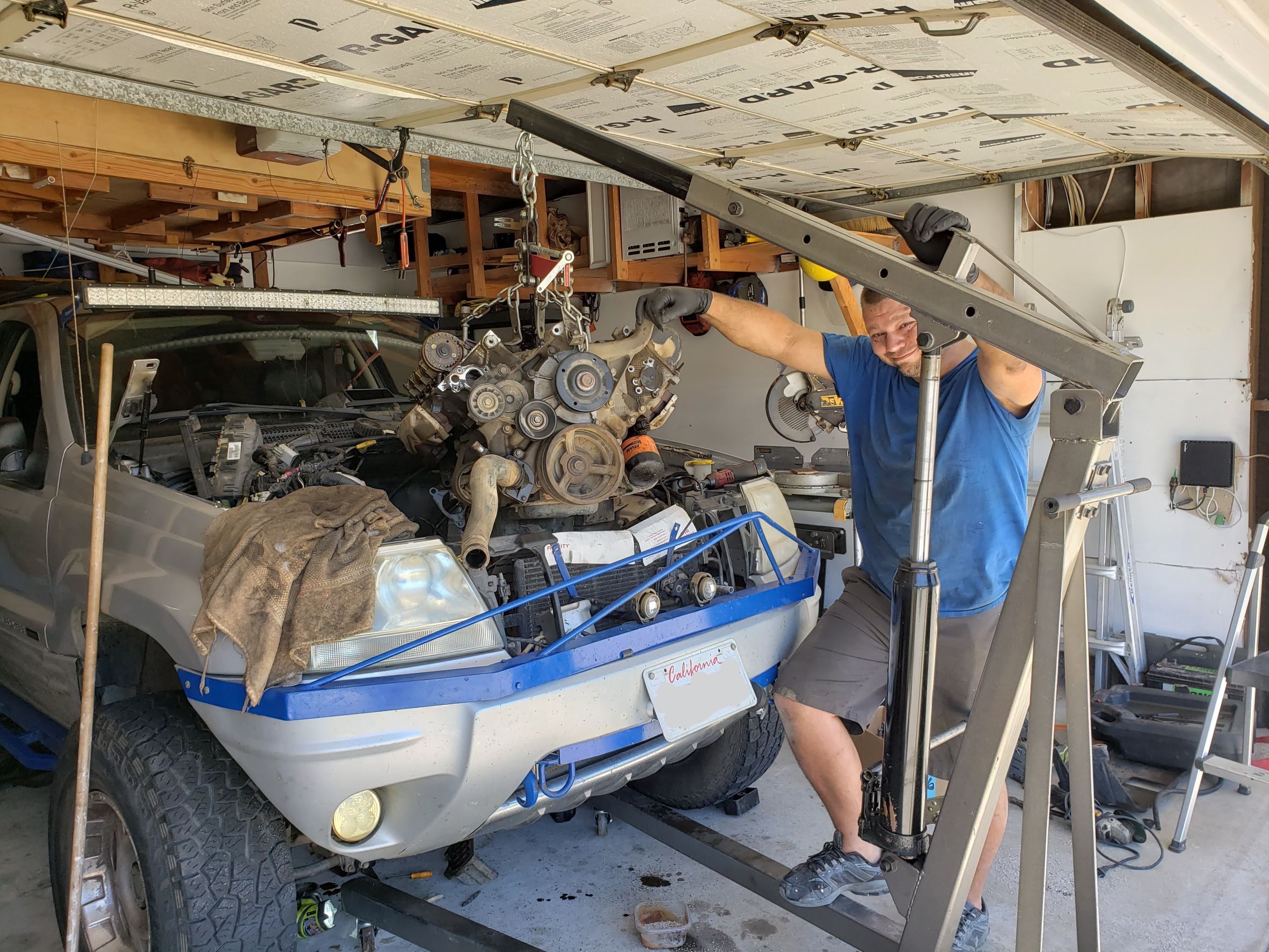 Jesse, the tech, with an engine hanging on a hoist just above a jeep